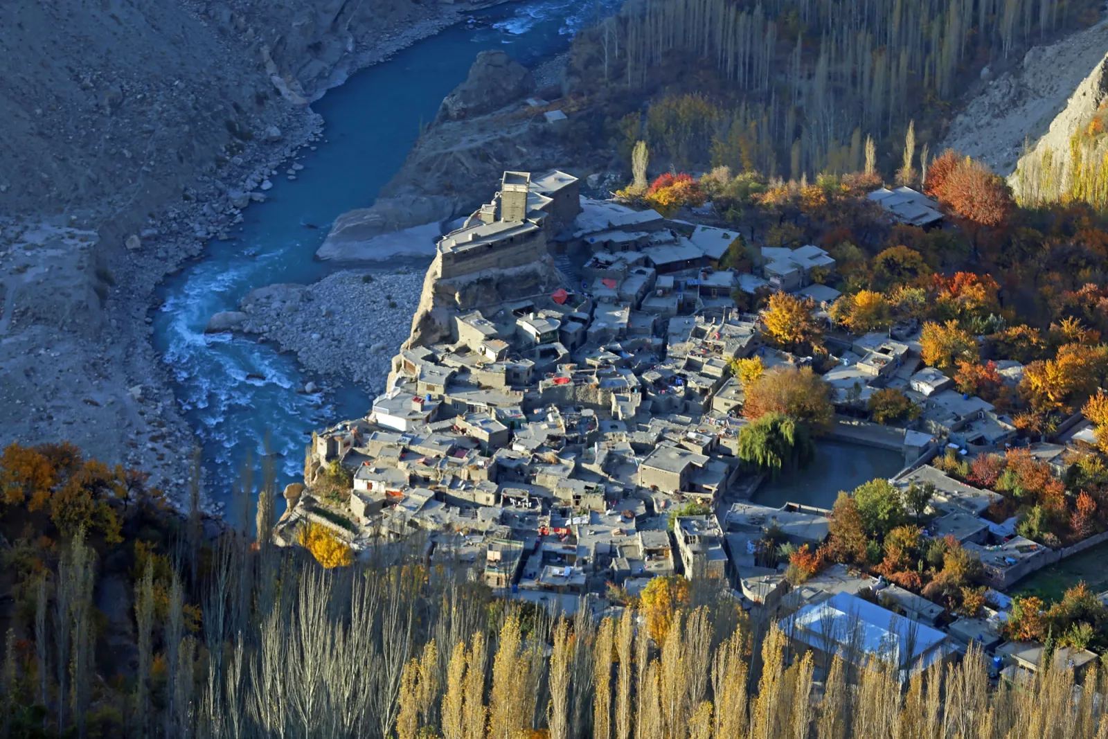 Altit Fort perched on a rock spur above the turquoise Hunza River, with the old village and autumn poplars below