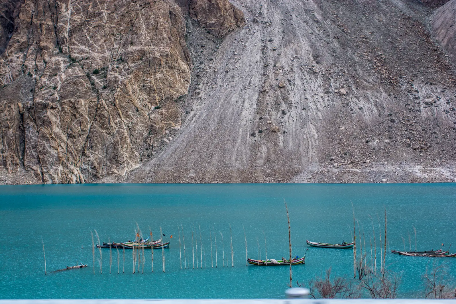 Wooden boats and the tops of drowned trees poking out of the turquoise water of Attabad Lake below the landslide scar, Gojal, Upper Hunza, Pakistan