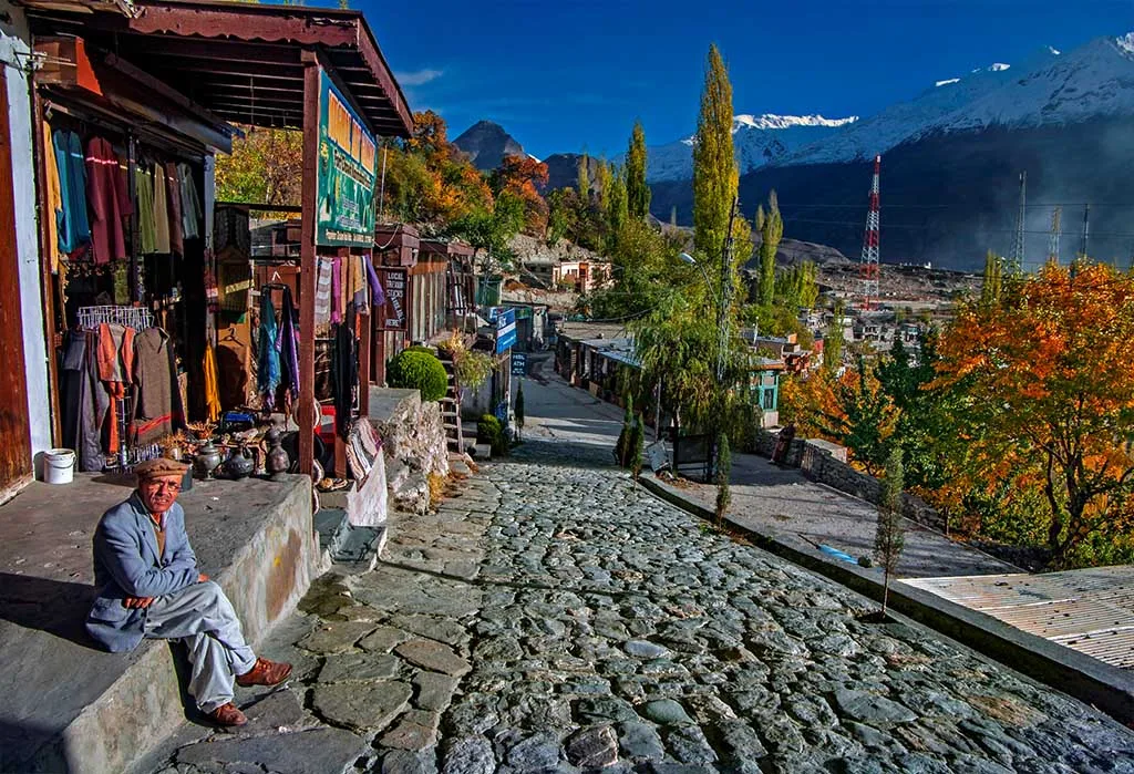 Old cobblestone bazaar street in Karimabad, Hunza, with autumn poplars and snow-capped Karakoram peaks