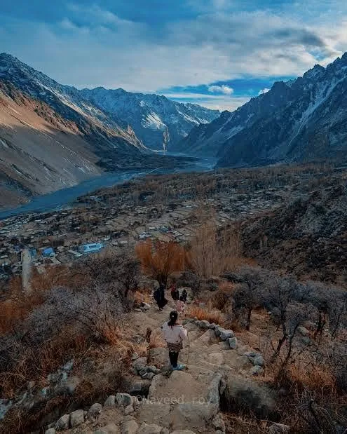 Hikers climbing the steep stone trail to the Ondra Poyga viewpoint above Gulmit, with the Gojal valley and glacier below