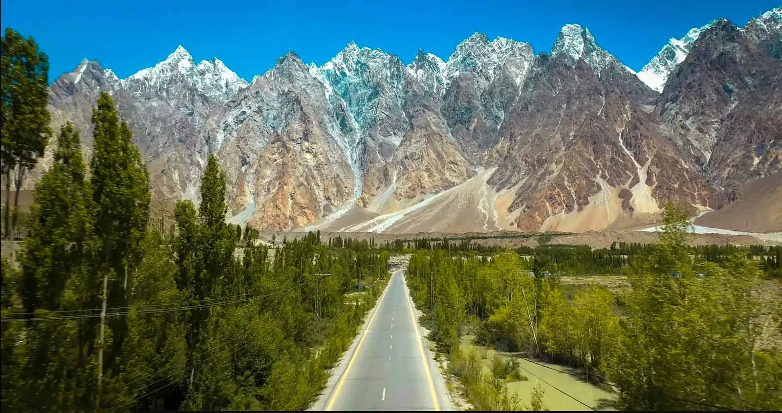 The saw-toothed Passu Cones (Tupopdan, 6,106 m) rising above the Karakoram Highway and green poplars near Passu village, Hunza