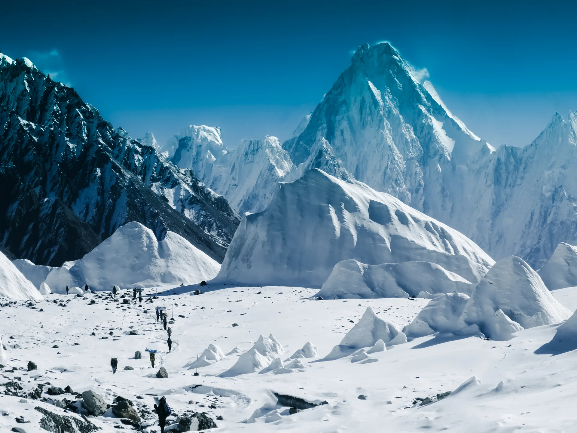 Trekkers crossing the upper Baltoro Glacier snowfield toward a Karakoram peak near Concordia on the K2 Base Camp trek