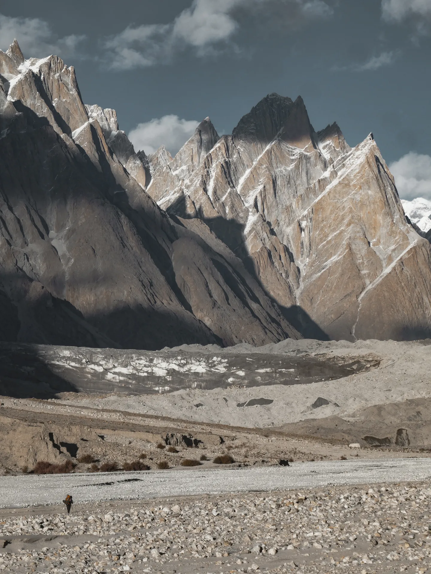 Granite spires above the Baltoro Glacier moraine on the trek to K2 Base Camp, with a porter crossing the gravel riverbed