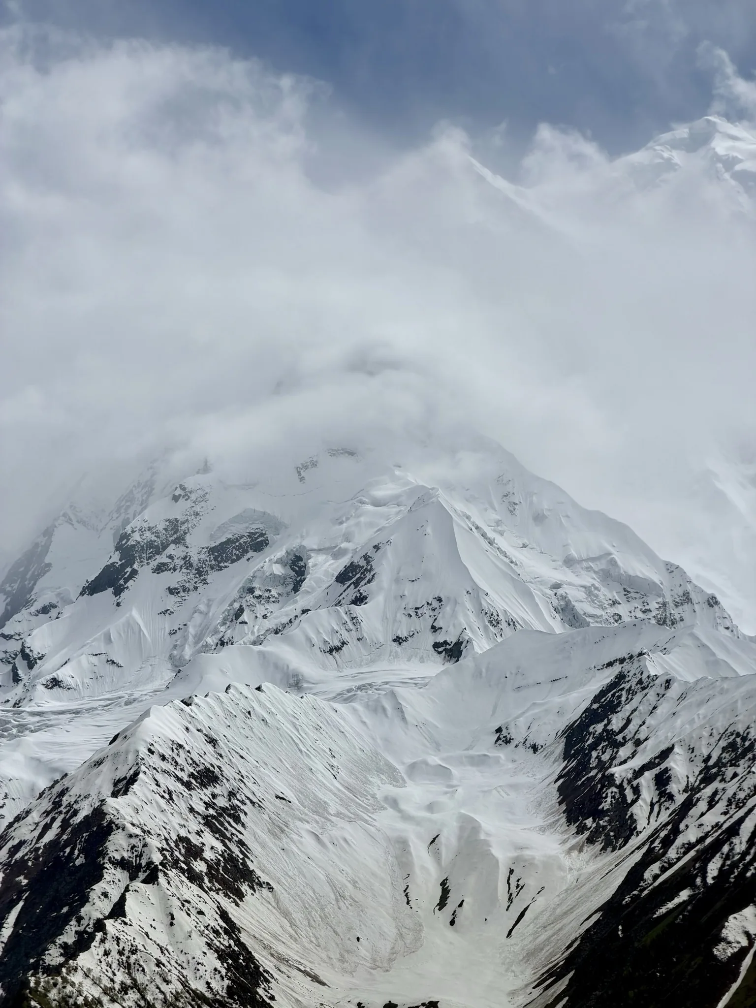 Rakaposhi's summit wreathed in cloud above steep snow slopes, Nagar Valley, Pakistan