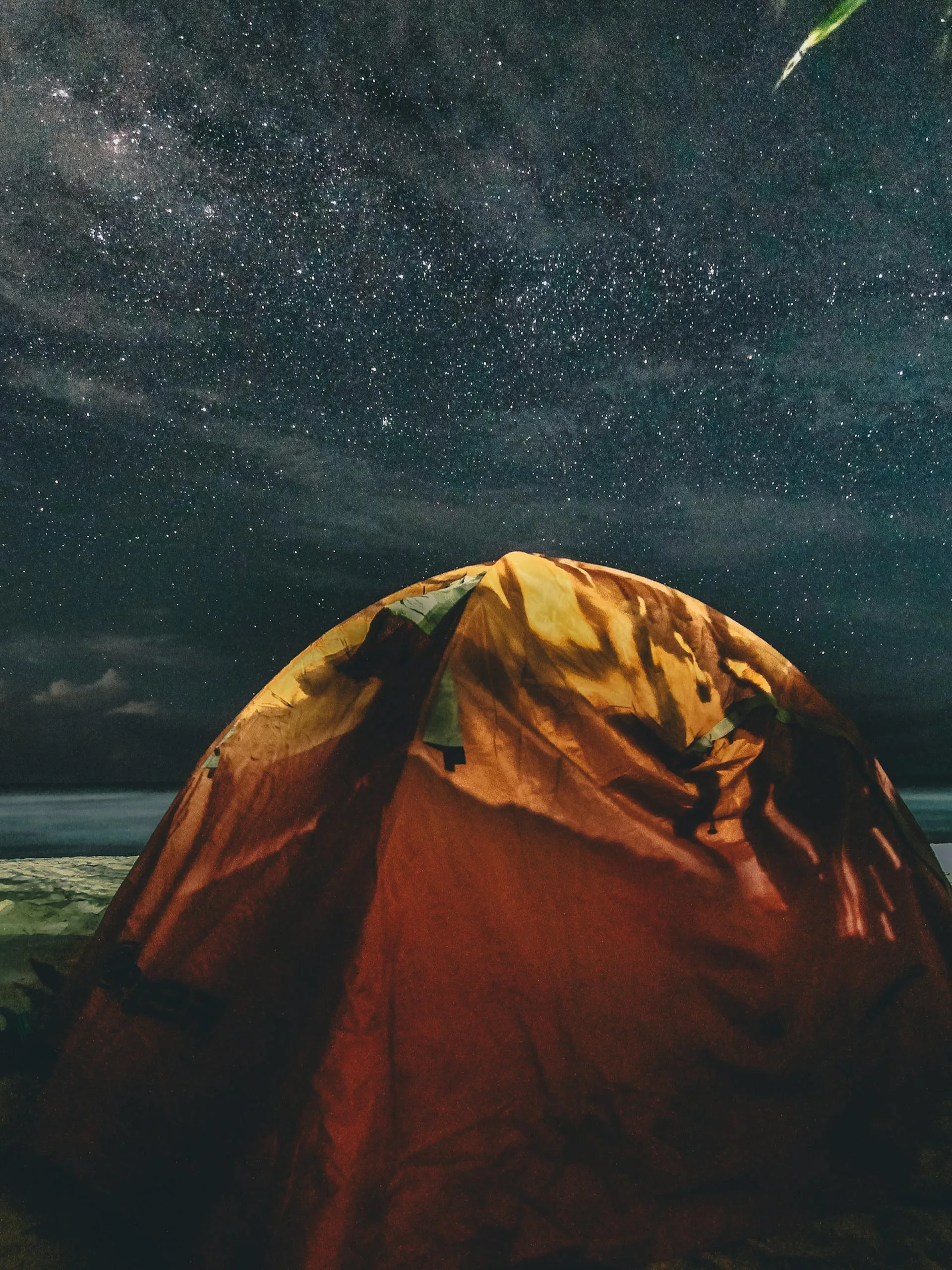 A glowing camping tent beneath a star-filled sky
