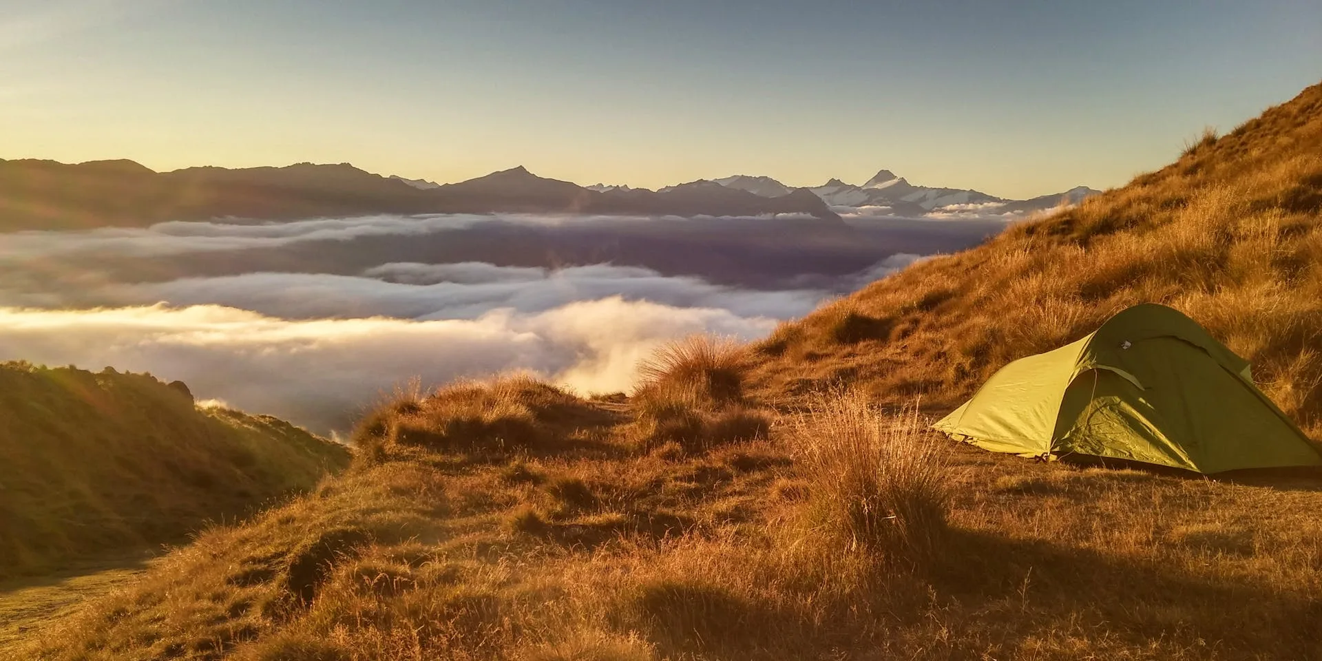 Tent on mountain top with sunrise over clouds