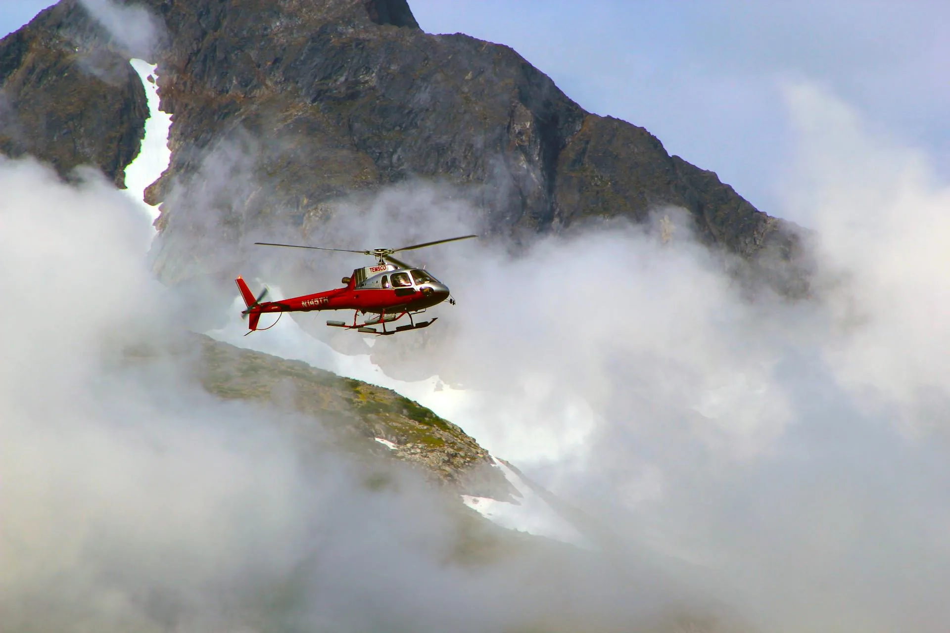 Red helicopter above foggy mountain peaks