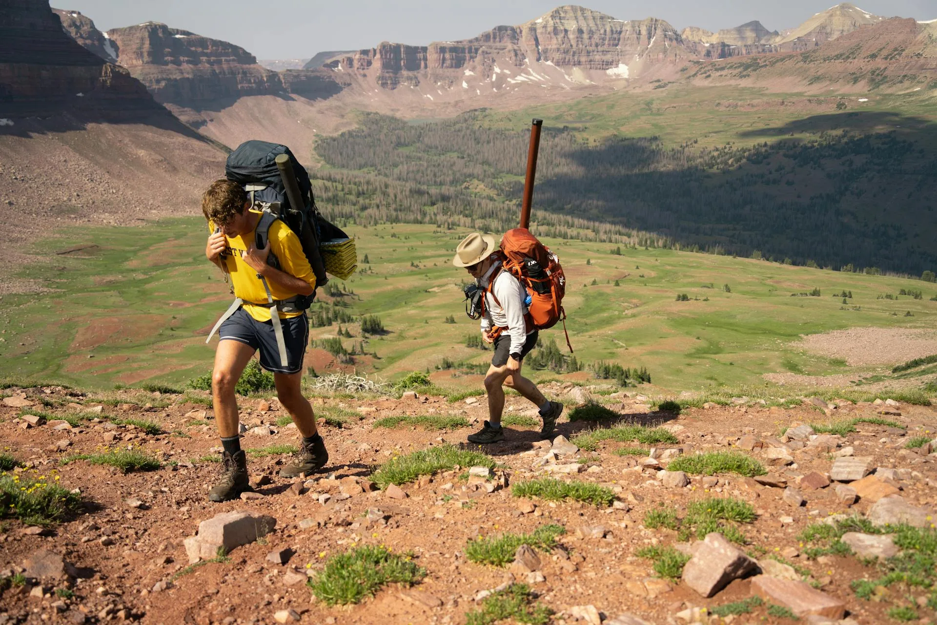 Two hikers with backpacks trekking up a mountain trail