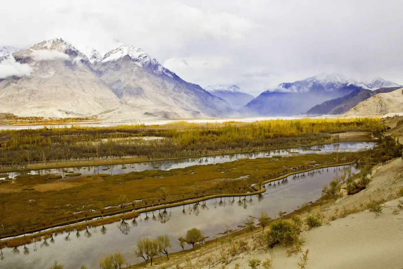 Anak sungai berliku melalui Lembah Skardu yang hijau di bawah puncak bersalji nipis